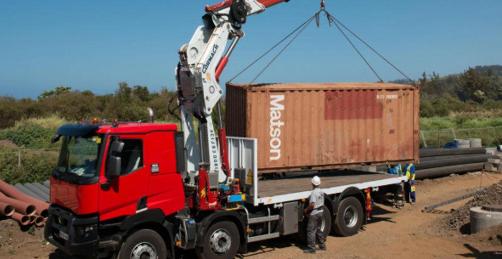 Camion-grue français déposant un conteneur maritime de 20 pieds sur terrain stabilisé, opérateur en gilet haute visibilité dirigeant la manœuvre
